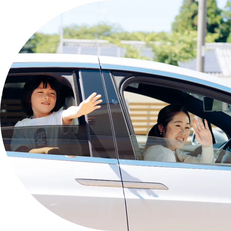 車の運転席に乗っている女性と後席に乗っている子供が手を振っている様子