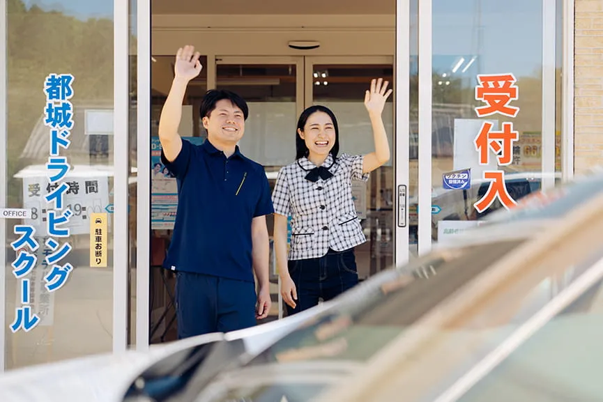 受付入り口から手を振る男性指導員と女性指導員