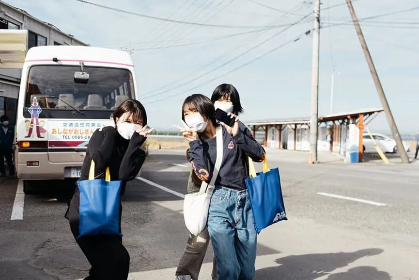 教習所のバスの前で楽しそうにピースする女性3人組の教習生
