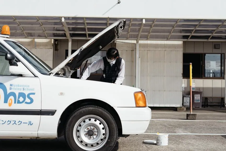 教習車のボンネットを開けて中を点検する女性指導員