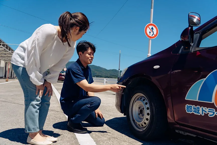 教習の出発前にタイヤの点検を男性指導員と女性教習生の様子