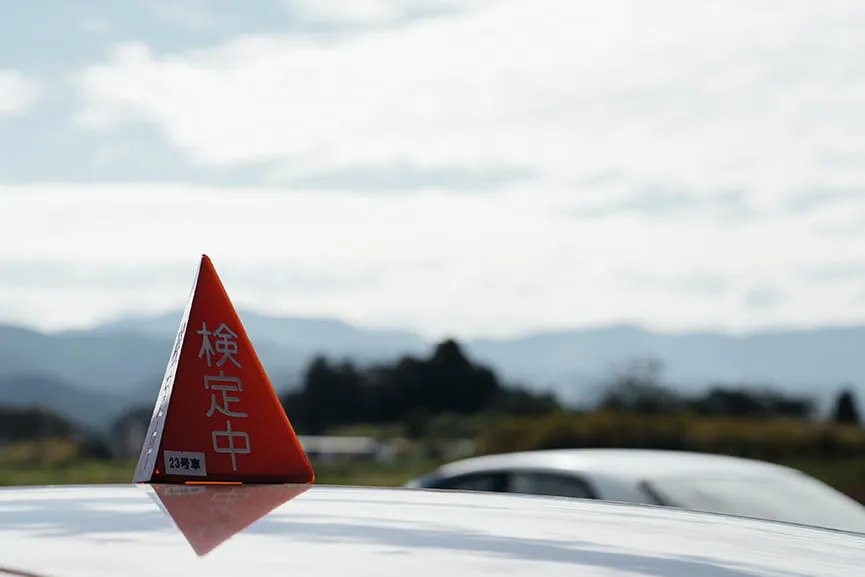 教習車のルーフに検定中と三角目印が立っている様子