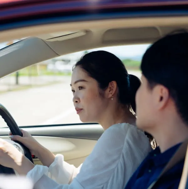 教習車で運転している女性教習生と助手席に乗って指導している男性指導員の様子