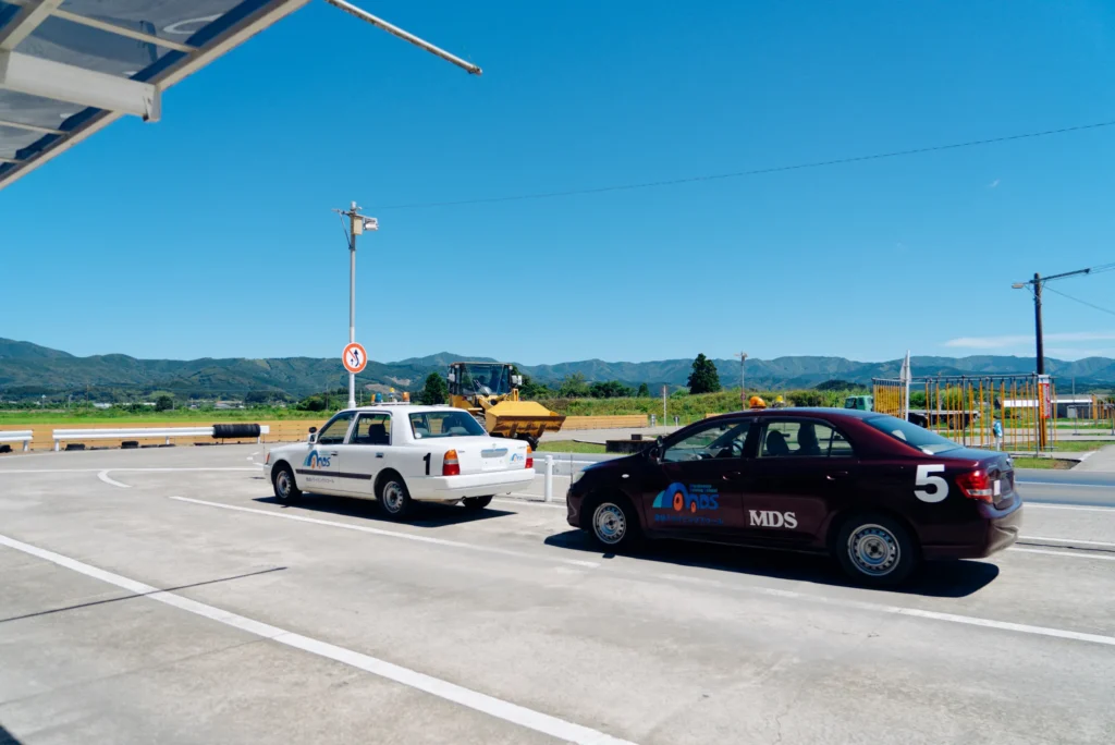 都城ドライビングスクールの教習コースに白い教習車と紫色の教習車が並んでいる様子