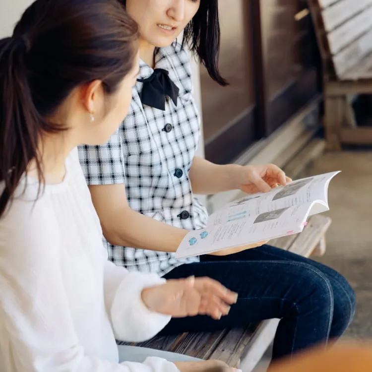 教習所内の長椅子に座って、テキストを説明している女性指導員とそれを聞いている女性教習生