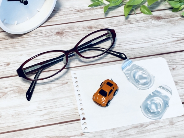 机の上に置かれているメガネとコンタクトとメモ帳とミニカー