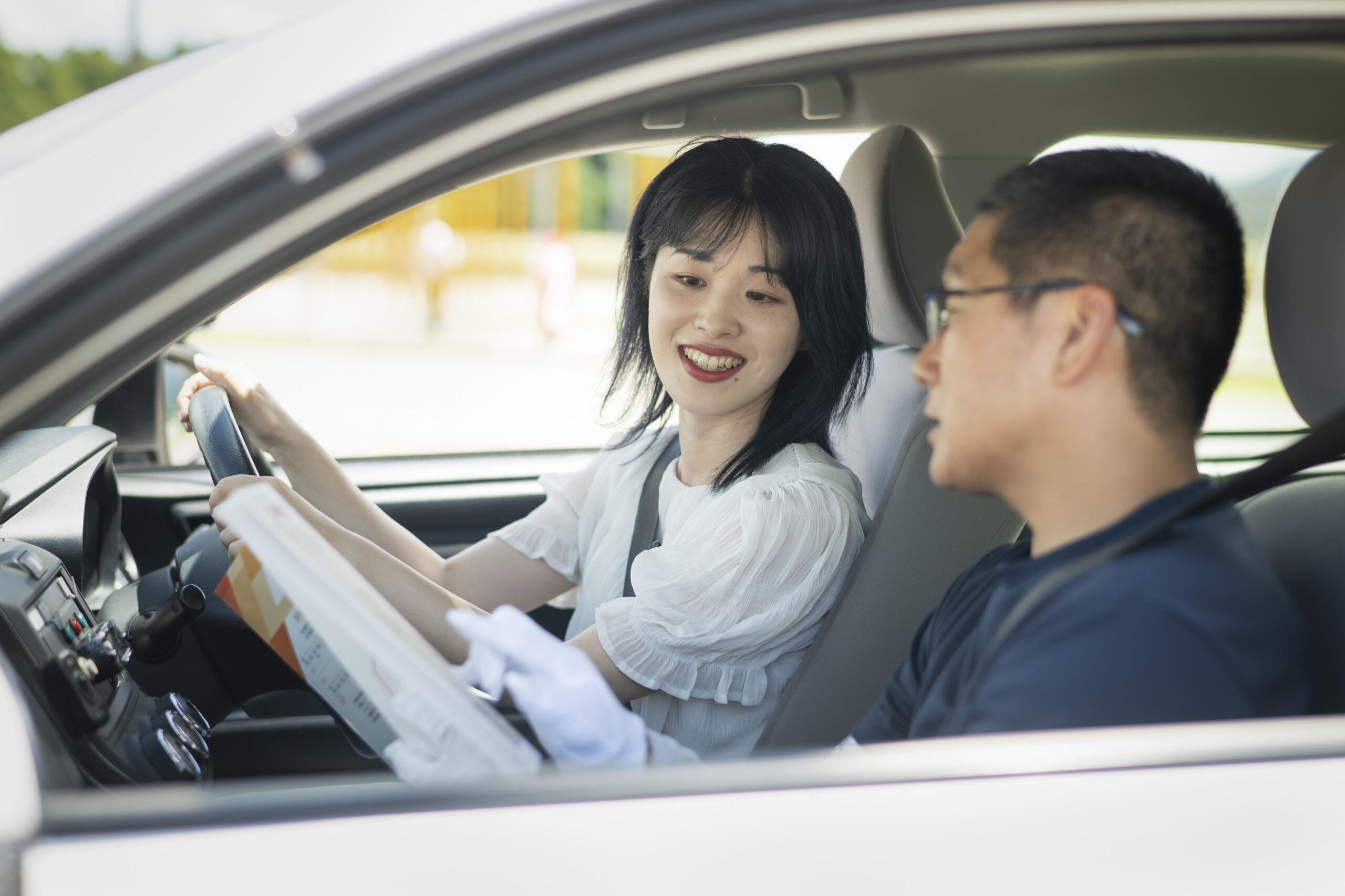 教習車内で男性教官から運転について説明をうけている女性教習生