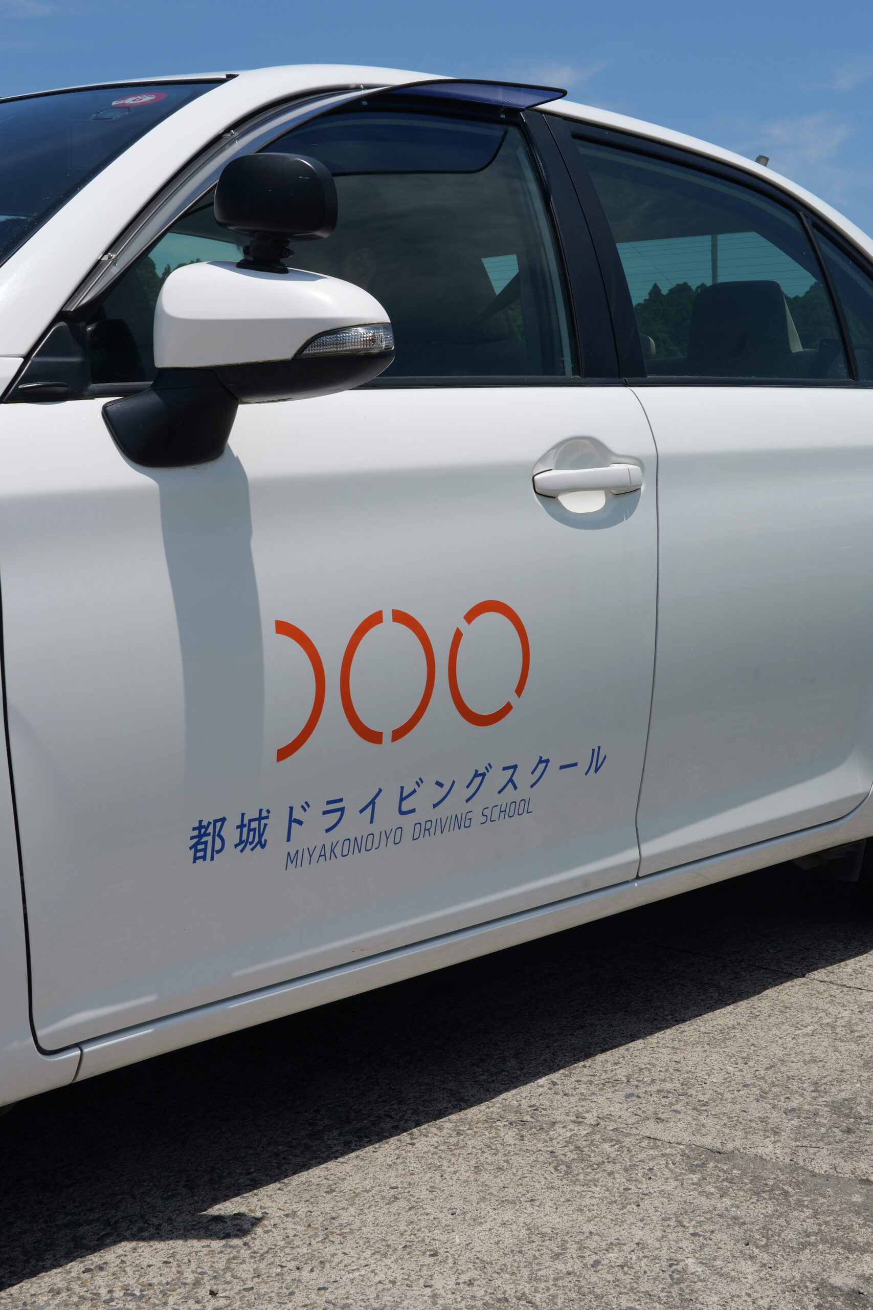 都城ドライビングスクールのロゴがドアにデザインされている白い教習車